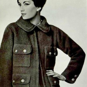 May include: A woman wearing a long, dark brown coat with large pockets and silver buttons. The coat has a collar and is made of a textured fabric.