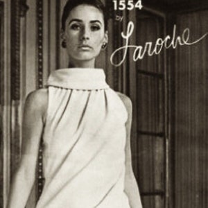 May include: A black and white photo of a woman wearing a white sleeveless dress with a high neck. The dress has a pleated design and is fitted. The woman is standing in front of a patterned wall and a wooden door. The text "1554 by Laroche" is visible in the top right corner of the image.