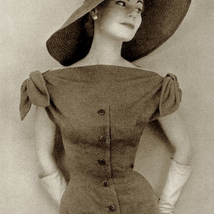 May include: A vintage sepia-toned photograph of a woman wearing a wide-brimmed hat with a bow and a button-down dress. The dress has short sleeves and a fitted waist. She is also wearing long gloves and a pearl earring.