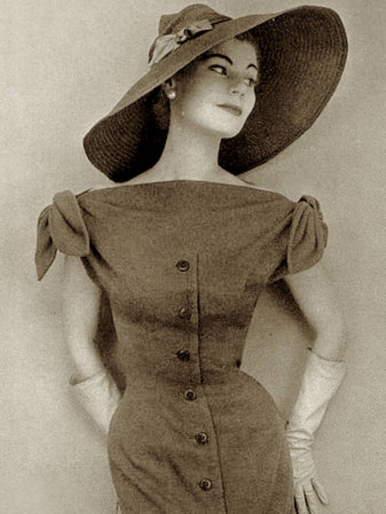 May include: A vintage sepia-toned photograph of a woman wearing a wide-brimmed hat with a bow and a button-down dress. The dress has short sleeves and a fitted waist. She is also wearing long gloves and a pearl earring.