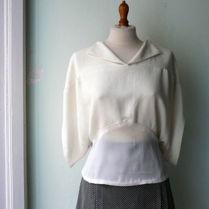 May include: A white blouse with a wide collar and long sleeves. The blouse has a fitted bodice and a loose, flowing skirt.
