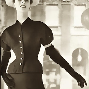 May include: A monochrome image of a vintage outfit. It features a black jacket with white buttons, short sleeves, and a matching skirt. The look is completed with long black gloves and a cream-coloured hat, creating a classic, elegant silhouette.