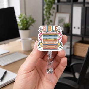 May include: A badge reel featuring a rectangular white plaque with the text BIBLE emergency numbers and a list of feelings paired with scripture references. The design is framed by colorful floral illustrations in pink, blue, and yellow tones.