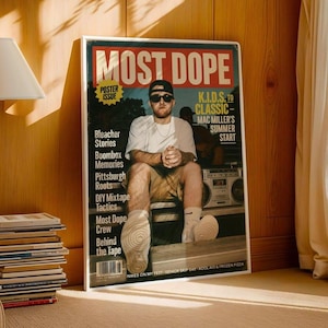 Op de afbeelding: Een ingelijste poster met de tekst "MOST DOPE" in grote letters. De poster toont een man met een zonnebril en een baseballpet, zittend voor een boombox. Extra tekst is onder meer "K.I.D.S. TO CLASSIC - MAC MILLER'S SUMMER START".