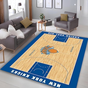 May include: A rectangular area rug featuring a basketball court design with the New York Knicks logo and team name. The rug has a blue border and a light brown court with blue and orange details. The rug is placed in a living room.