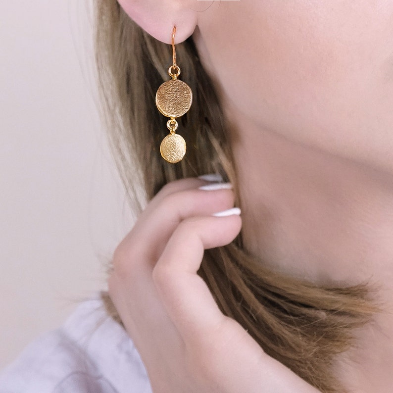 May include: Gold-toned dangle earrings with two round discs. The larger disc is textured and the smaller disc is smooth.