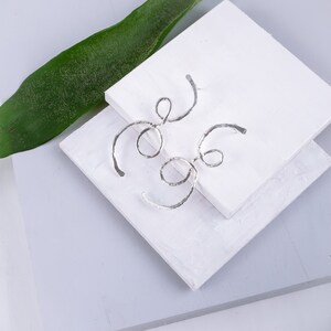 May include: A pair of silver earrings with a unique, abstract design. The earrings are made of thin, twisted wire and have a textured finish.