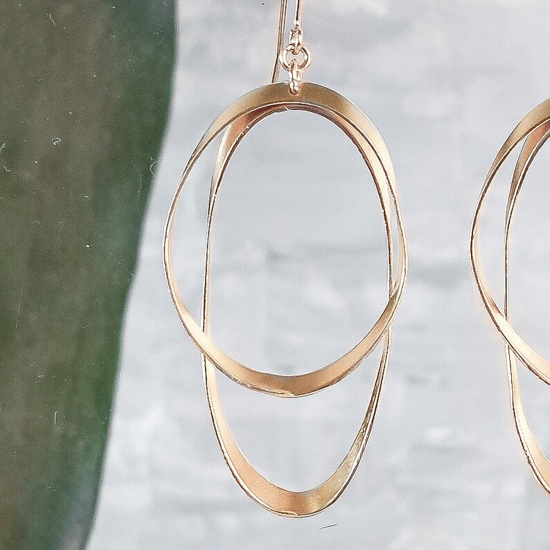 May include: Gold-toned double hoop earrings with a simple, modern design. The earrings are made of two interlocking hoops, one slightly larger than the other.