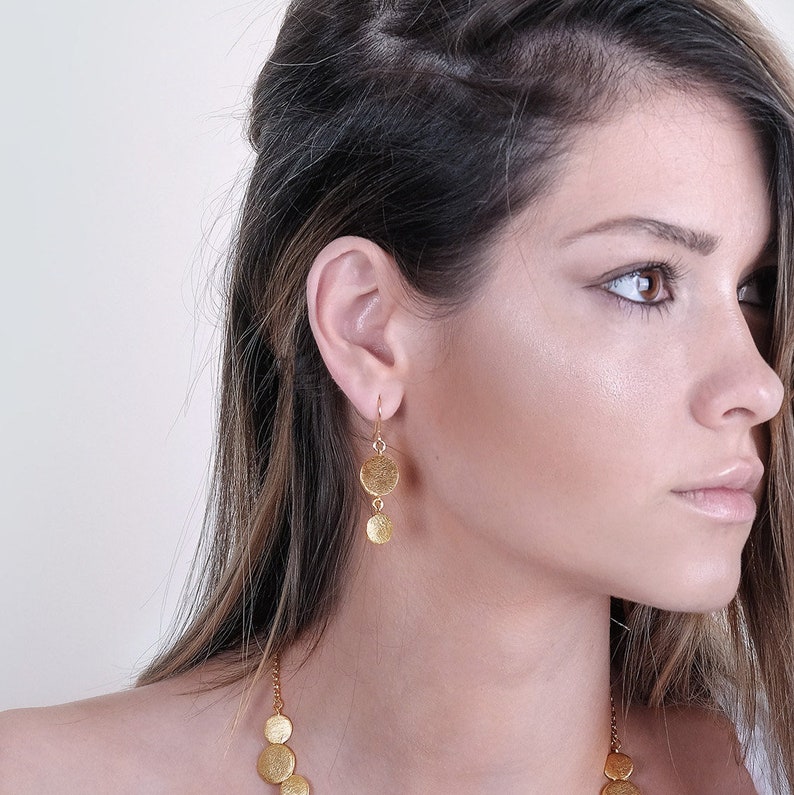 May include: Gold dangle earrings with three round discs. The discs have a textured surface.