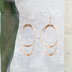 May include: A pair of gold-toned earrings featuring a double circle design. The earrings are crafted from two overlapping circles, creating a contemporary and minimalist style.