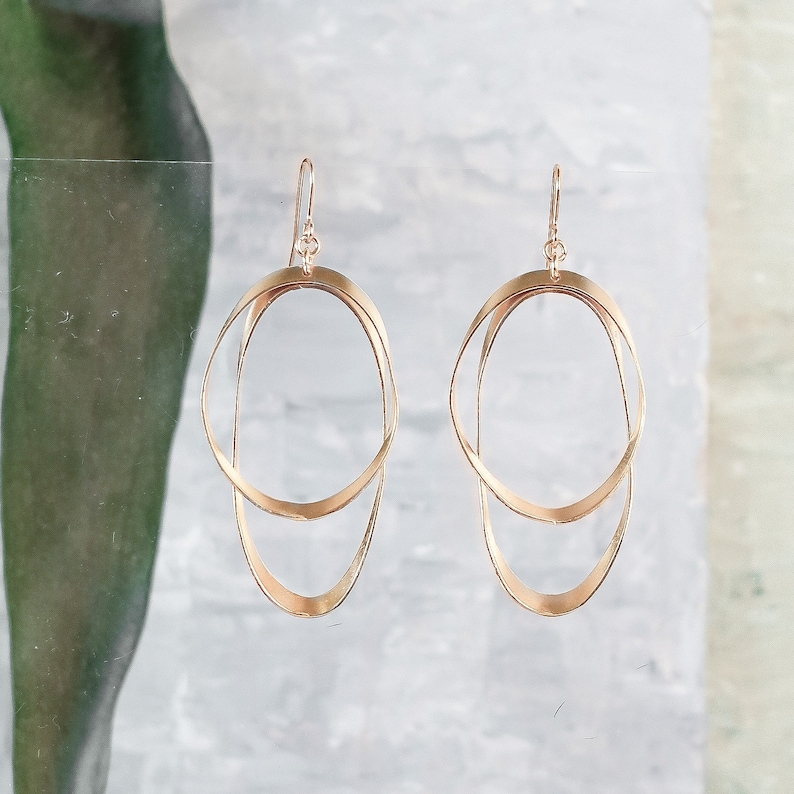 May include: A pair of gold-toned earrings featuring a double circle design. The earrings are crafted from two overlapping circles, creating a contemporary and minimalist style.