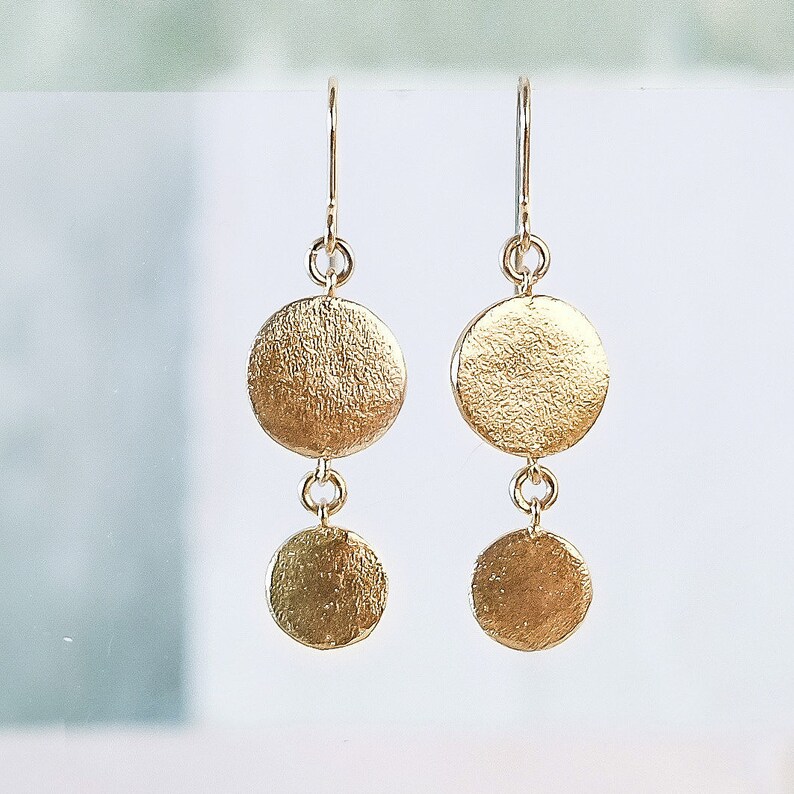 May include: Gold dangle earrings with two round discs on each earring. The discs have a textured, hammered finish.