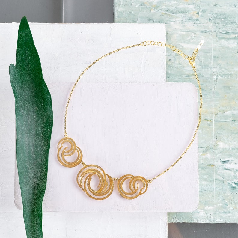 May include: A gold necklace with a chain and three circular pendants. The pendants are made of interlocking circles.