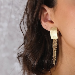 May include: Gold-toned rectangular earrings with a textured surface and cascading chain fringe. The earrings are a warm gold color and are worn on the ear. The earrings are a statement piece.