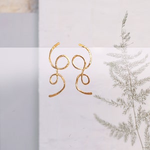 May include: A pair of gold-toned earrings with a unique, abstract design. The earrings are made of thin, twisted wire that forms a series of loops and curves.
