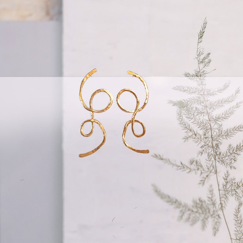 May include: A pair of gold-toned earrings with a unique, abstract design. The earrings are made of thin, twisted wire that forms a series of loops and curves.