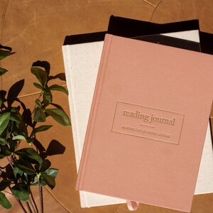 May include: A pink reading journal with the text "reading journal" and "A book log for book lovers" embossed in gold on the front cover.