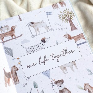 May include: An open book with a light blue and white patterned cover featuring watercolor illustrations of dogs on skateboards, scooters, and kites. The text "our life together" is displayed in a cursive font.