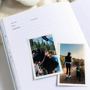 May include: Open journal with lined pages and prompts for Activity, Date, and Highlights. Two photos are attached: one of a person with a black dog, and another of a person hiking with a black dog. The journal is open on a white surface.