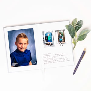 K&ouml;nnte beinhalten: Ein wei&szlig;es Fotoalbum mit einem blauen Hintergrundfoto eines Jungen, der ein blaues Hemd tr&auml;gt. Das Album ist auf einer Seite mit einer handschriftlichen Nachricht und zwei kleineren Fotos des Jungen vor einer Schule ge&ouml;ffnet.