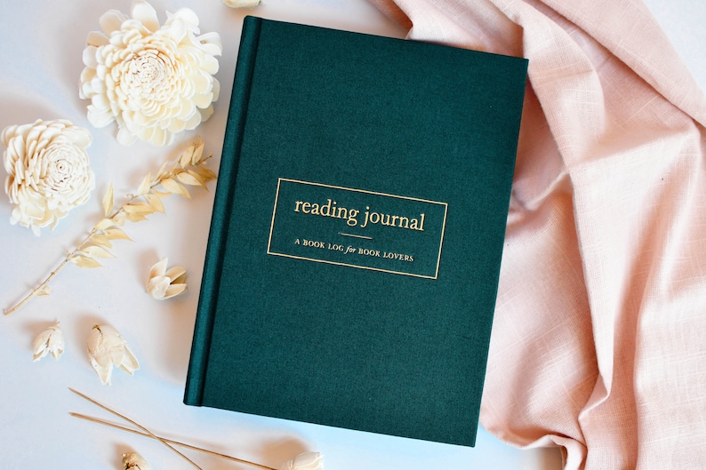 K&ouml;nnte beinhalten: Ein dunkelgr&uuml;nes Hardcover-Journal mit goldener Beschriftung, die "reading journal" und "A BOOK LOG for BOOK LOVERS" lautet.