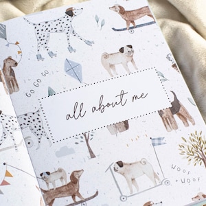May include: Open book with a patterned cover featuring illustrations of various dog breeds, kites, and trees. The text "all about me" is centered on a white dotted rectangle. The background is a soft, neutral color.