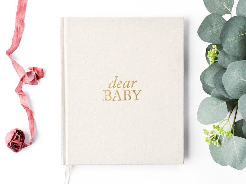 May include: A white journal with the words "dear baby" in gold lettering on the front cover.
