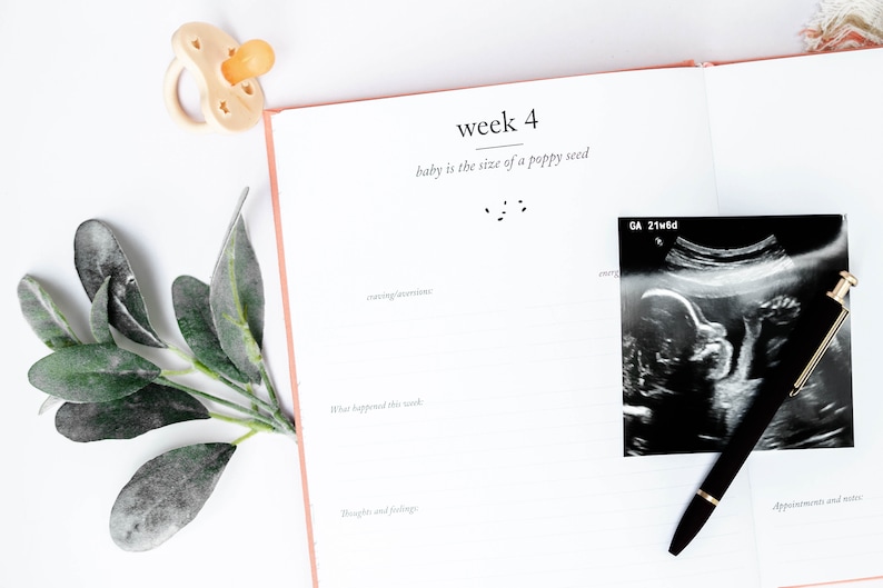 May include: A white pregnancy journal with the text "week 4" and "baby is the size of a poppy seed". A black and white ultrasound image is on the right side of the page with a black pen on top of it.