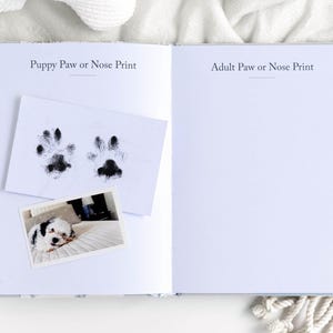 May include: Open book with the text "Puppy Paw or Nose Print" and "Adult Paw or Nose Print". A small photo of a puppy is on the left page, along with a print of two puppy paw prints. The right page is blank.