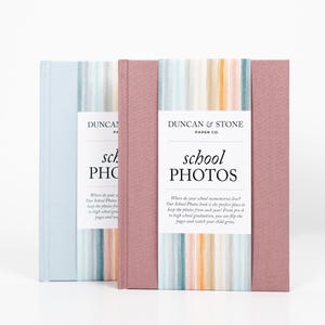 K&ouml;nnte beinhalten: Zwei Fotoalben mit gestreiften Umschl&auml;gen. Das Album links ist hellblau mit einem wei&szlig;en Etikett, auf dem "Duncan & Stone Paper Co. school PHOTOS" steht. Das Album rechts ist rosa mit einem wei&szlig;en Etikett, auf dem "Duncan & Stone Paper Co. school PHOTOS" steht.