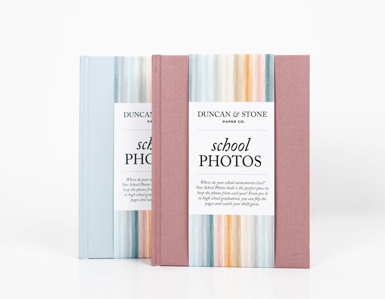 K&ouml;nnte beinhalten: Zwei Fotoalben mit gestreiften Umschl&auml;gen. Das Album links ist hellblau mit einem wei&szlig;en Etikett, auf dem "Duncan & Stone Paper Co. school PHOTOS" steht. Das Album rechts ist rosa mit einem wei&szlig;en Etikett, auf dem "Duncan & Stone Paper Co. school PHOTOS" steht.