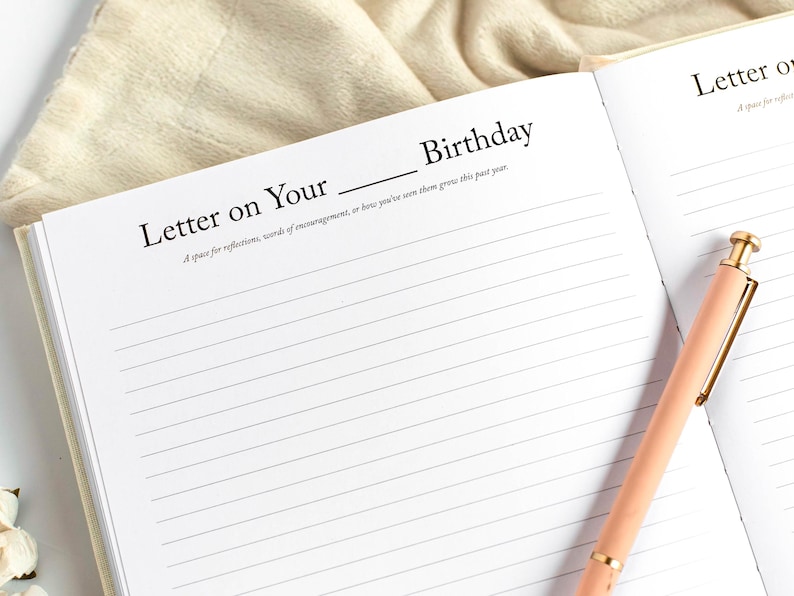 May include: Open journal with lined pages and the text "Letter on Your Birthday." A peach-colored pen with gold accents rests on the right page. The journal is open on a light-colored surface.