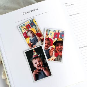 May include: An open journal with the text "the occasion:" and lined pages. Three photos are placed on the page, featuring a baby wearing a party hat and balloons. The journal is open on a white surface.