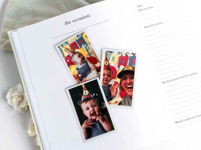 May include: An open journal with the text "the occasion:" and lined pages. Three photos are placed on the page, featuring a baby wearing a party hat and balloons. The journal is open on a white surface.