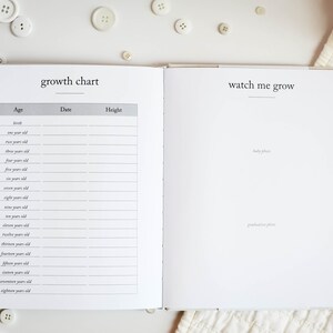 May include: A white baby book with a growth chart on the left page and a "watch me grow" section on the right page. The growth chart has columns for age, date, and height. The right page has space for baby photos and graduation photos.