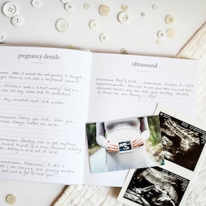 May include: A white journal with a black cover and the words "pregnancy details" and "ultrasound" written on the front. The journal is open to two pages, one with handwritten notes about pregnancy cravings and the other with a photo of a pregnant woman holding an ultrasound image and two ultrasound images.