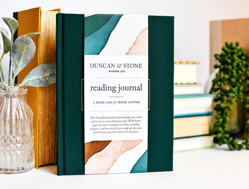 K&ouml;nnte beinhalten: Ein gr&uuml;nes Lesetagebuch mit dem Titel "reading journal" und dem Text "A BOOK LOG for BOOK LOVERS" auf dem Cover. Das Cover zeigt au&szlig;erdem ein Aquarelldesign mit abstrakten Formen in Blaut&ouml;nen, Gr&uuml;n- und Oranget&ouml;nen.