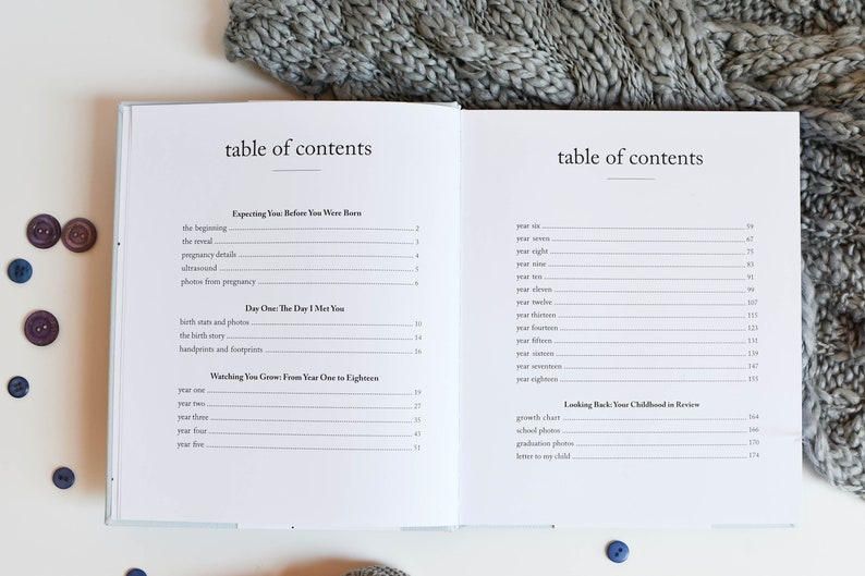 May include: A white book with a blue cover and the title "table of contents" printed on the front. The book is open to a page with a table of contents for a baby memory book. The table of contents includes sections for "Expecting You Before You Were Born", "Day One: The Day I Met You", "Watching You Grow: From Year One to Eighteen", and "Looking Back: Your Childhood in Review".