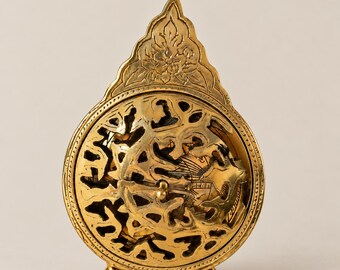 May include: A gold-colored brass spherical incense burner featuring an intricate openwork lattice design. The top is adorned with a pointed, floral-engraved finial, and the entire structure is supported by three small, rounded ball feet.