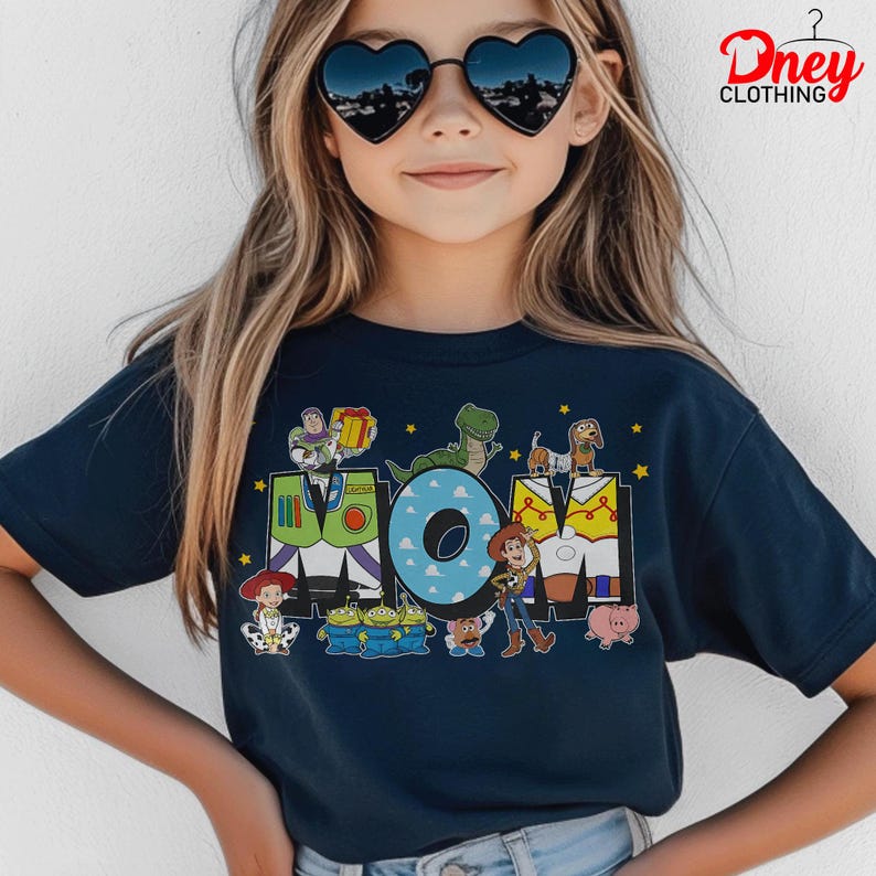 May include: Navy blue t-shirt with the word "MOM" and Toy Story characters. The "M" is designed as Buzz Lightyear's suit, the "O" has a blue sky pattern, and the "M" is designed as Woody's vest. The shirt has a crew neck.