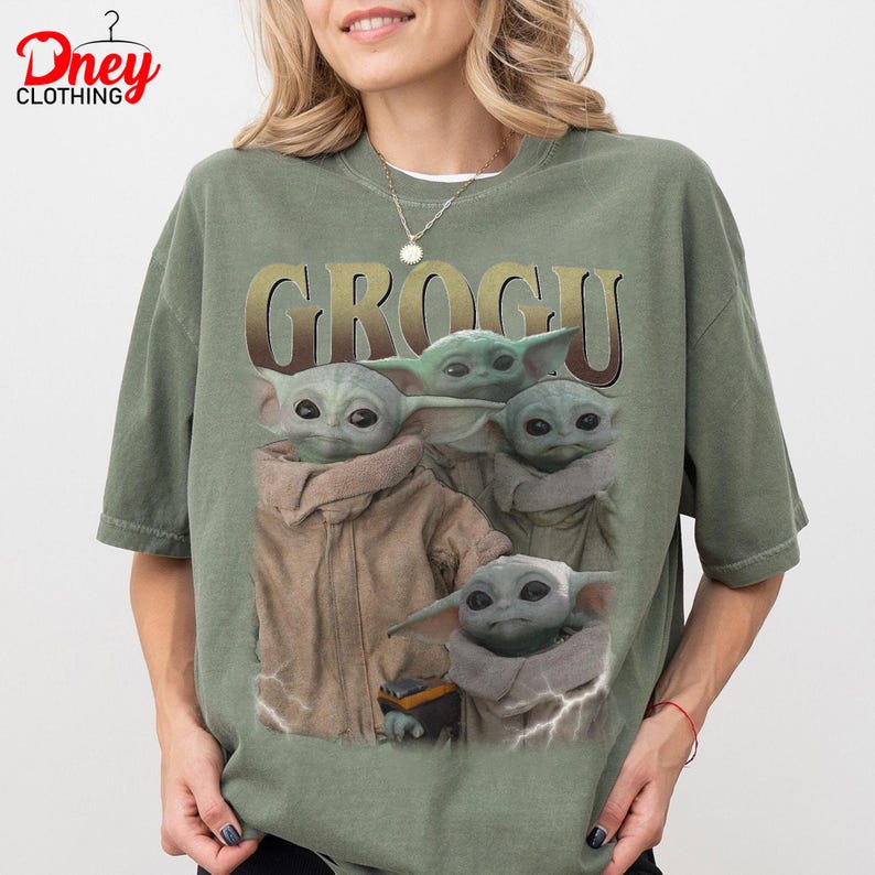 K&ouml;nnte beinhalten: Ein olivgr&uuml;nes T-Shirt mit dem Wort "GROGU" in goldfarbenen Buchstaben. Das Shirt zeigt eine Grafik von Grogu, auch bekannt als Baby Yoda, aus der Star Wars-Serie. Die Grafik zeigt Grogu in verschiedenen Posen.