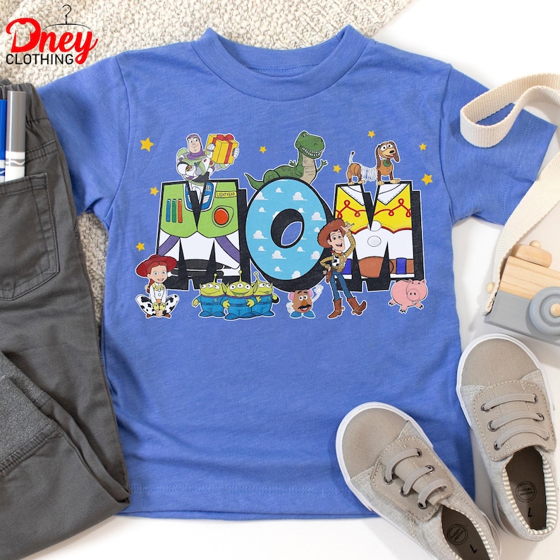 May include: A light blue t-shirt with the word "MOM" and Toy Story characters. The "M" is designed as Buzz Lightyear's suit, the "O" has a blue cloud pattern, and the "M" is designed as Woody's vest. Other characters include Rex, Slinky Dog, and the Little Green Men.