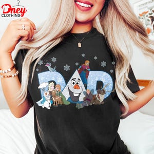 May include: Black t-shirt featuring the word "DAD" in light blue with snowflake accents and cartoon characters. The shirt has a crew neck and a graphic design of characters from a popular animated movie.