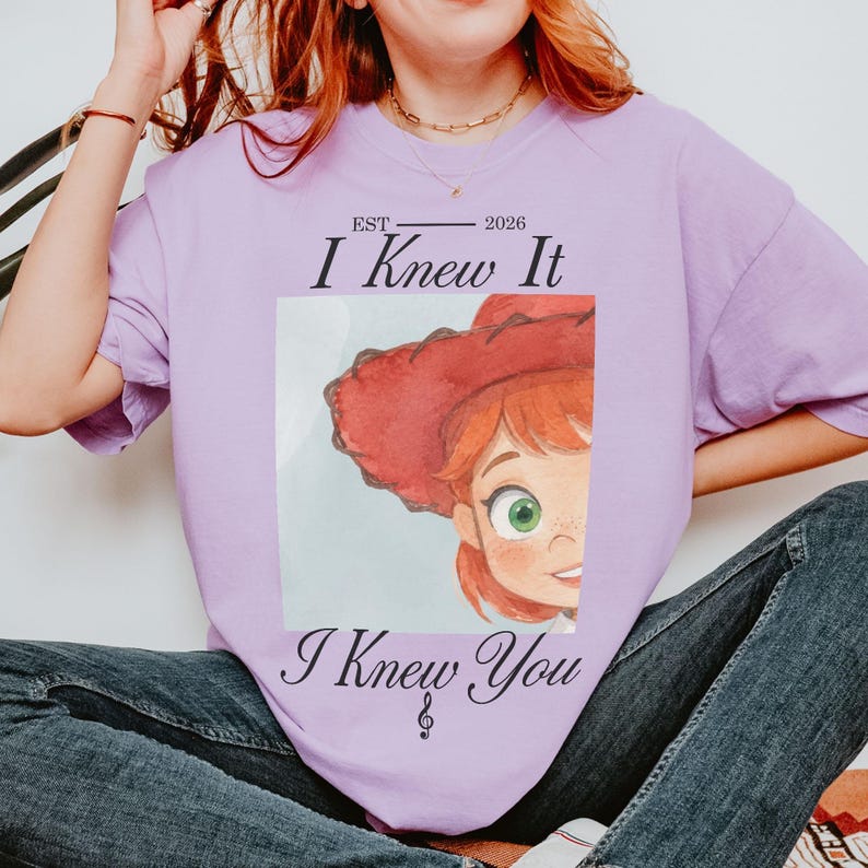 Puede incluir: Una camiseta de color morado claro con un gr&aacute;fico de un personaje con sombrero rojo y ojos verdes. El texto dice EST 2026 I Knew It I Knew You con un s&iacute;mbolo de clave de sol. El dise&ntilde;o est&aacute; centrado en el pecho de la prenda de manga corta.