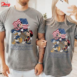 May include: Two grey t-shirts with a patriotic design featuring Mickey, Donald, and Minnie Mouse in colonial outfits. They hold a flag and drum. The text reads "250 Years of Freedom" and "United States Semiquincentennial 1776-2026".