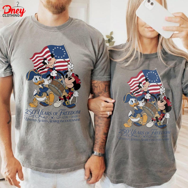 May include: Two grey t-shirts with a patriotic design featuring Mickey, Donald, and Minnie Mouse in colonial outfits. They hold a flag and drum. The text reads "250 Years of Freedom" and "United States Semiquincentennial 1776-2026".