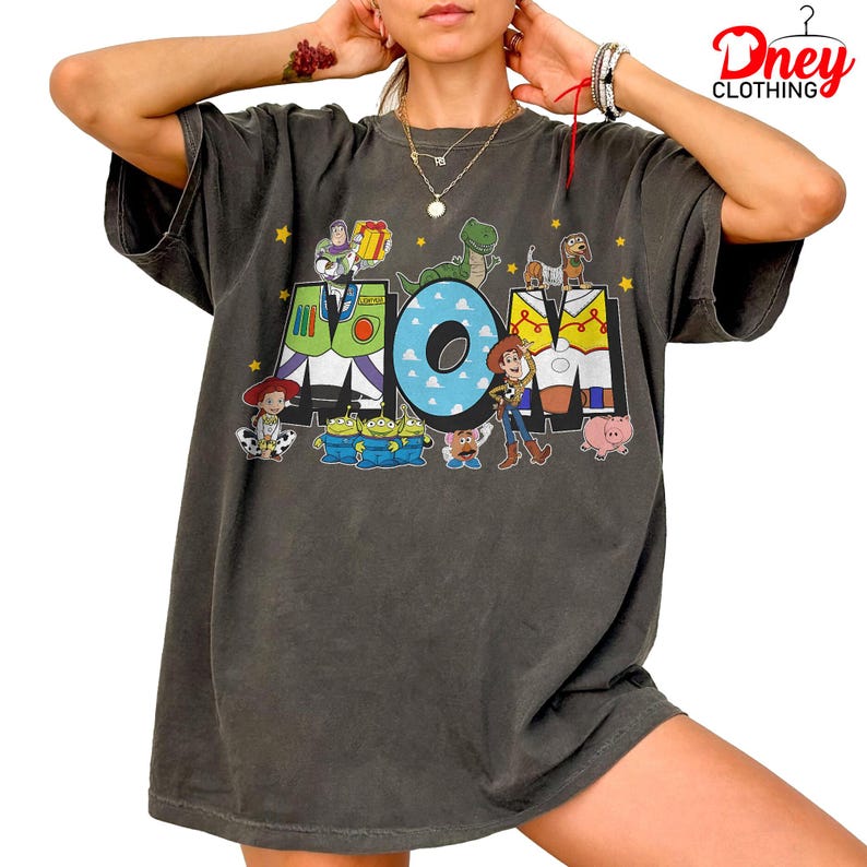 May include: Dark grey t-shirt with the word "MOM" and Toy Story characters. The "M" is green and white, the "O" is blue, and the "M" is yellow and white. The shirt has a loose fit.