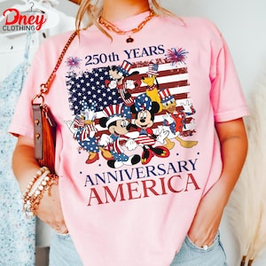 Puede incluir: Camiseta rosa claro con un dise&ntilde;o que celebra el 250 aniversario de Am&eacute;rica. El dise&ntilde;o presenta personajes de Disney y la bandera estadounidense. El texto dice "250th YEARS ANNIVERSARY AMERICA".