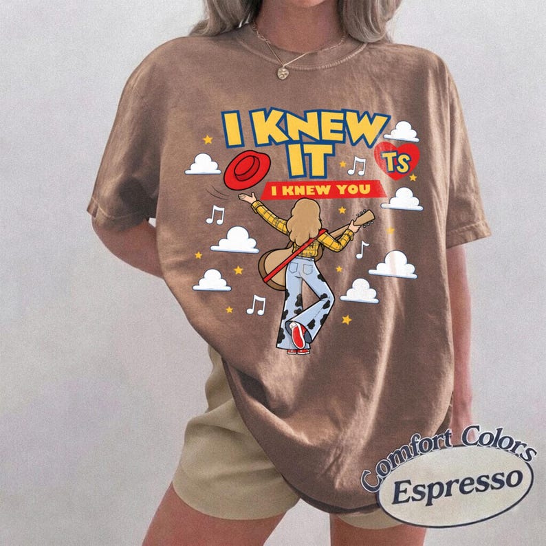 K&ouml;nnte beinhalten: Ein braunes T-Shirt mit einer Grafik einer Person mit langem Haar, die eine Akustikgitarre spielt und ein gelbes Karohemd sowie eine Hose mit Kuhfleckenmuster tr&auml;gt. Der Text lautet I KNEW IT und I KNEW YOU, umgeben von Wolken, Sternen und Noten.