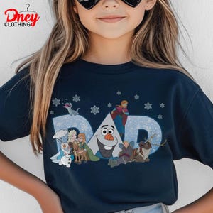 May include: Navy blue t-shirt with the word "DAD" in light blue, featuring characters from the movie Frozen. The design includes Olaf, Anna, Elsa, Kristoff, Sven, and snowflakes. The shirt has the "Dney Clothing" logo.